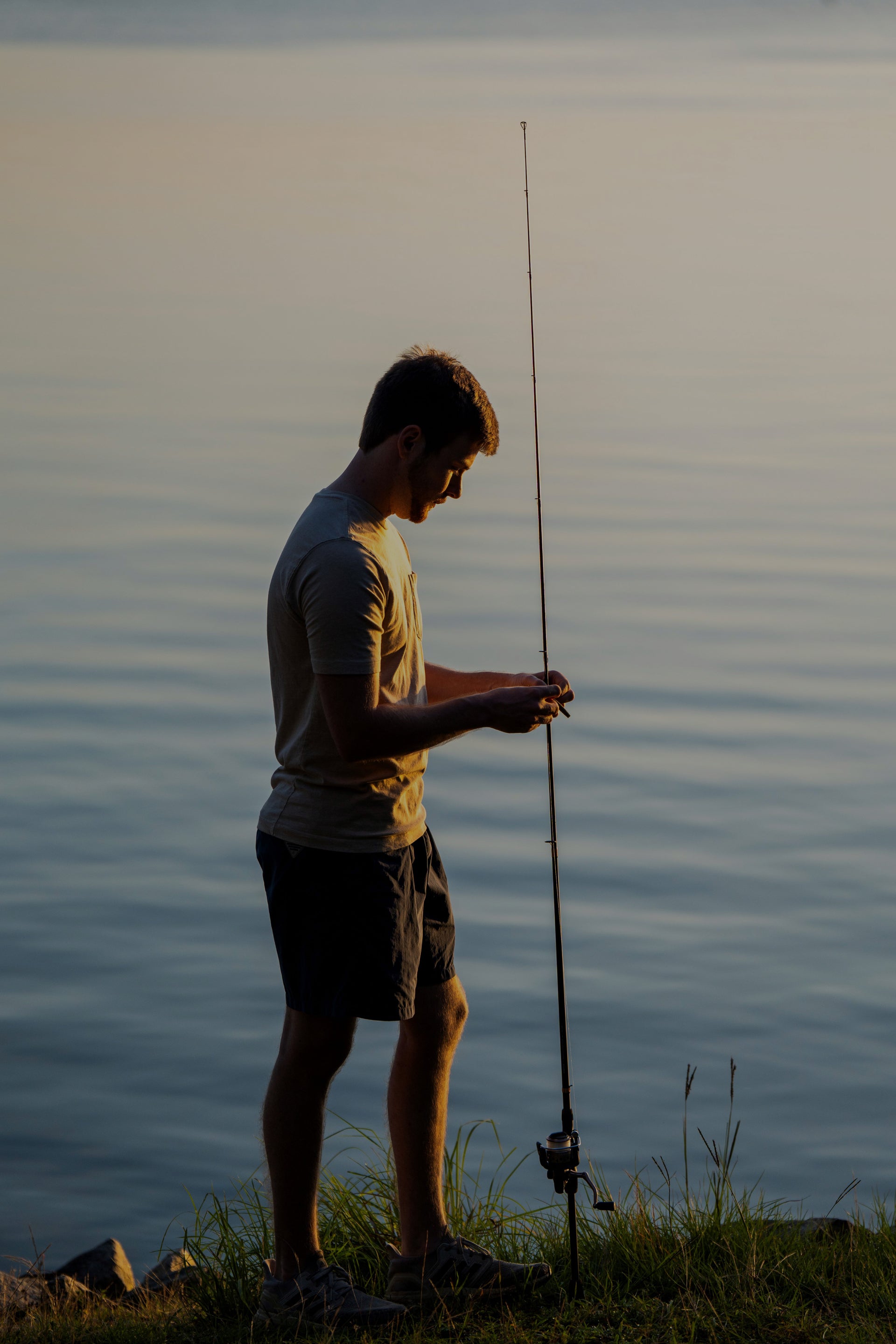 Man fishing by a lake at sunset