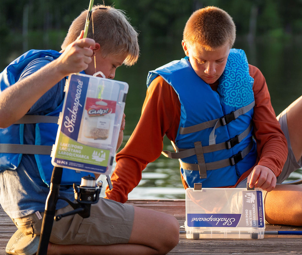 Two boys with fishing gear on a dock by a body of water.