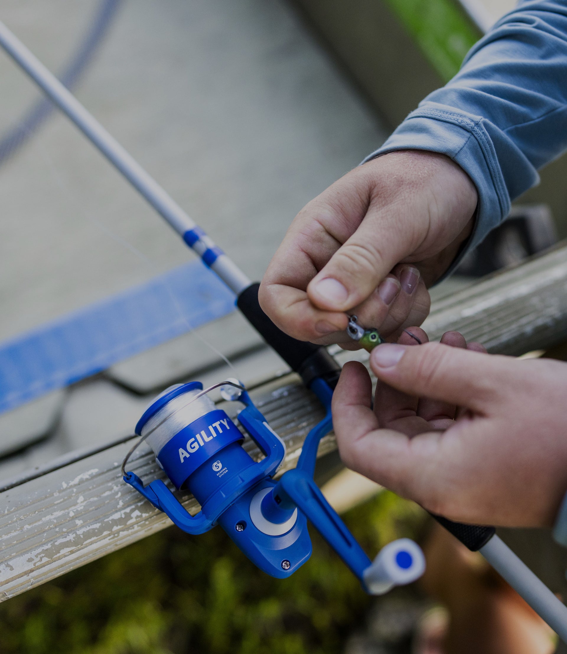 Person adjusting a blue Aglio reel on a fishing rod with a blurred background